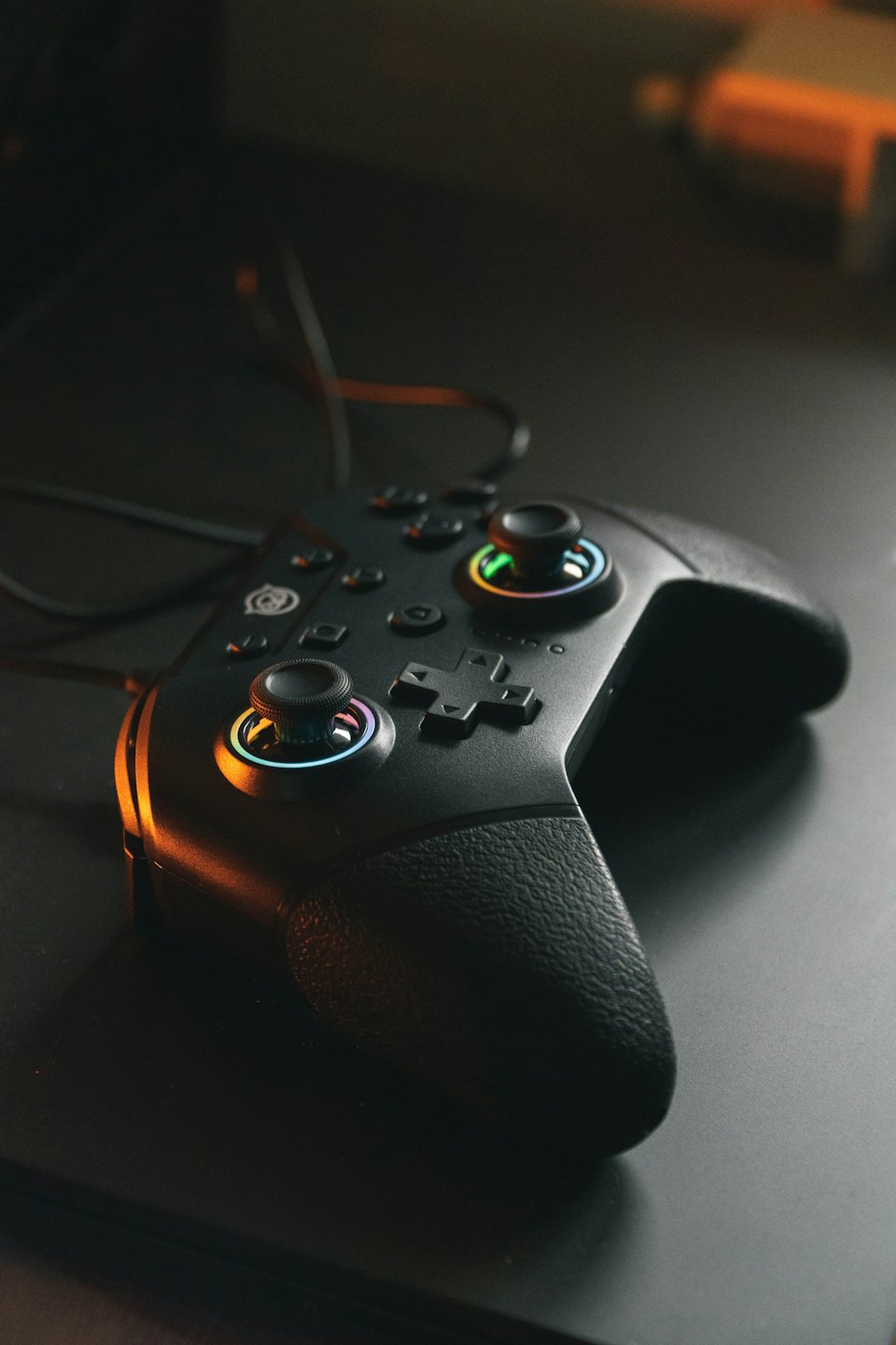 A black gaming controller with glowing colorful joysticks.