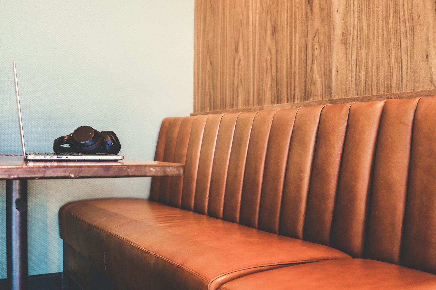 Laptop and headphones on a wooden table by a leather booth.